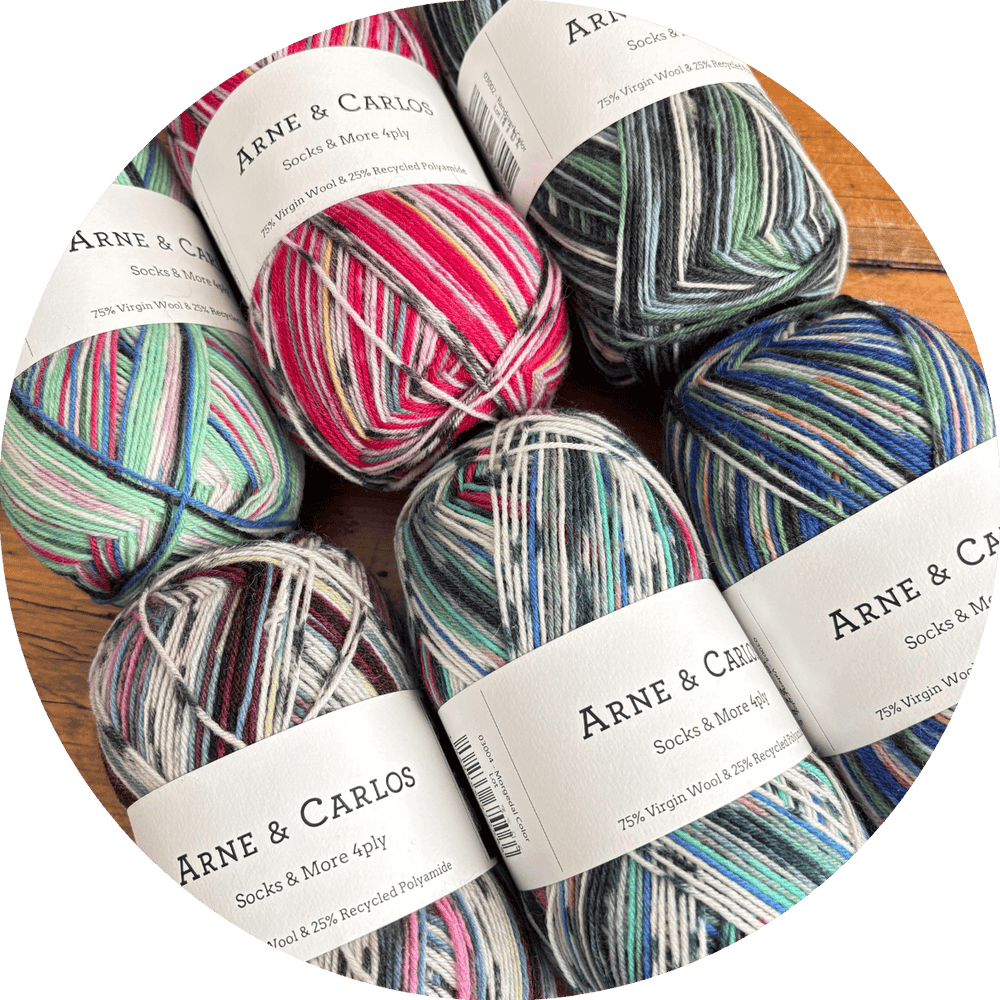 Colorful, variegated yarn balls with 'Arne & Carlos Socks & More 4ply' labels on a wooden surface.