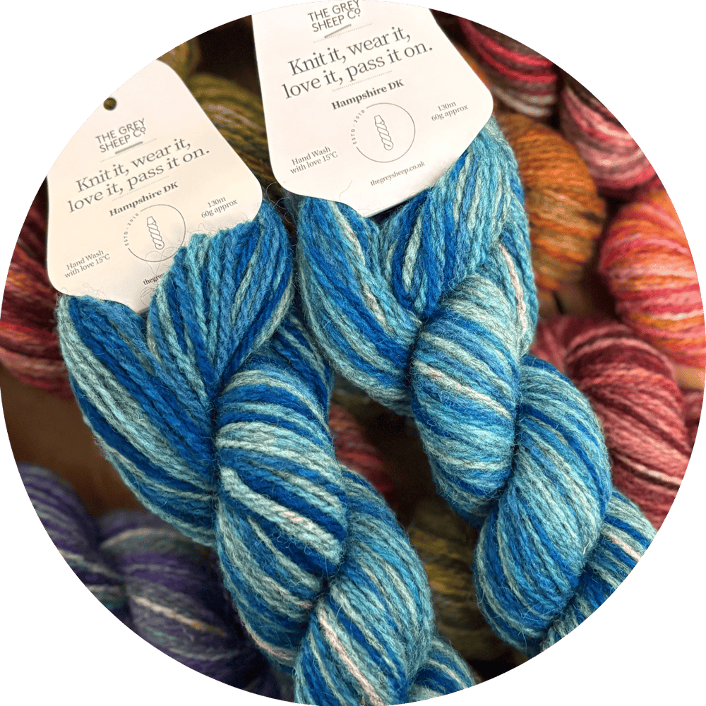 Two skeins of blue yarn with tags on a background of other multicolored skeins.