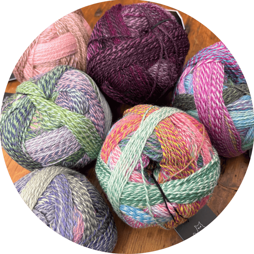 Colorful, variegated balls of yarn on a wooden surface. Yarn is Zauberball Crazy and labels are outside of frame.