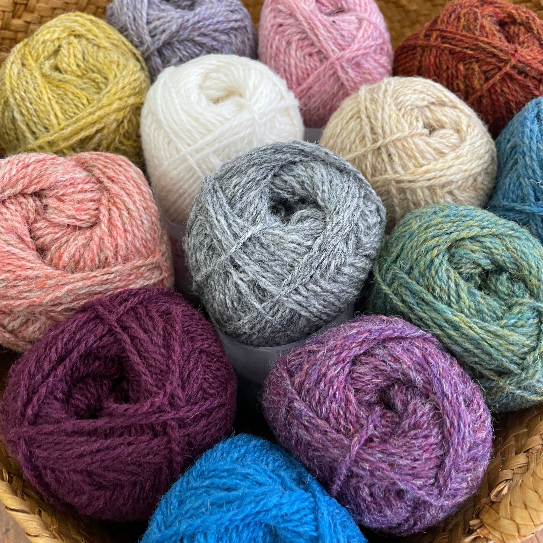 Jamieson & Smith 2ply Jumper Weight Wool Yarn in various colors arranged in basket. Viewed from above.