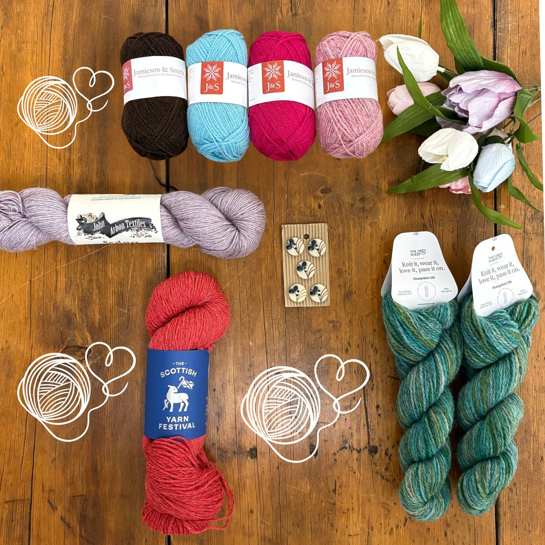 The yarns included in the Spring Taster Box spread out on a wooden surface. 3 yarn drawings indicate the yarns that are a secret. 
