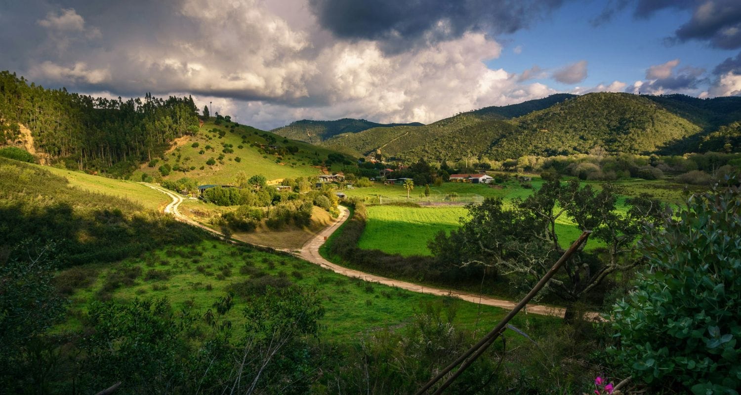 wide range landscape view of green land with cloudy sky. house in distance.