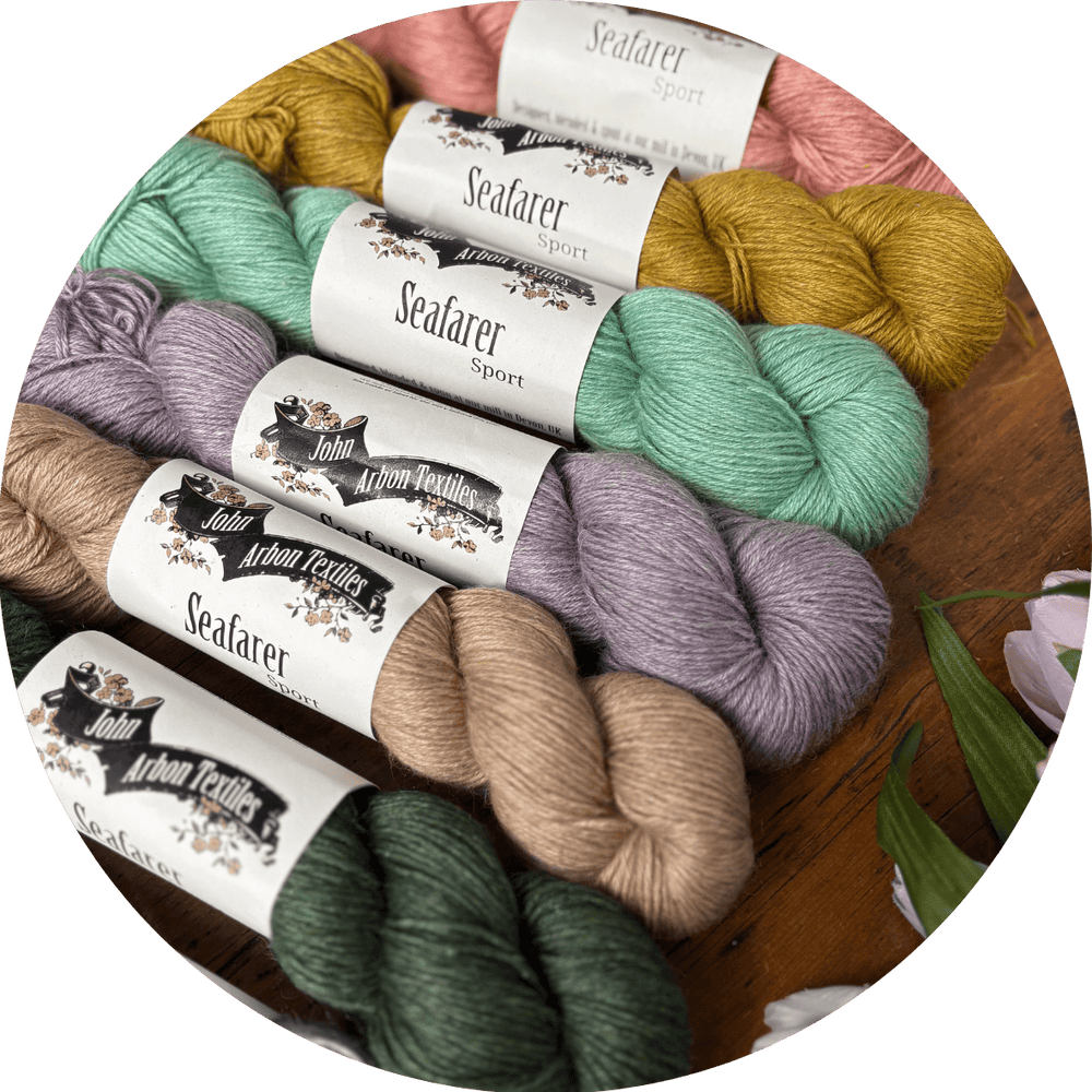 Light colored skeins of yarn with 'Joh Arbon Textiles Seafarer Sport' labels on a wooden surface.