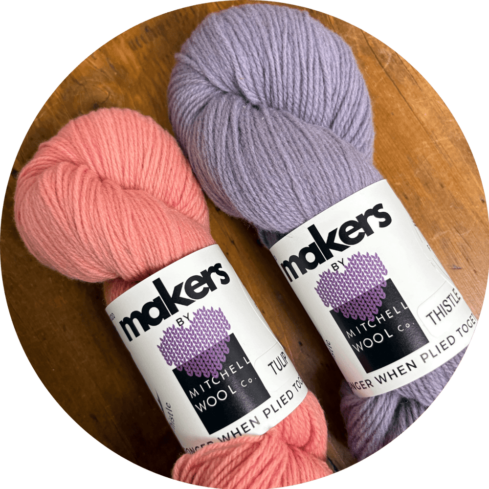 Two Skeins of pink and purple yarn with labels Makers by Mitchell Wool Co. shown on wooden surface.