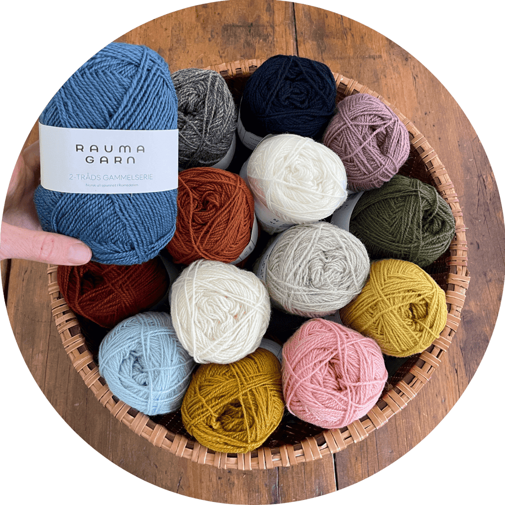 Basket of colorful yarn balls with a hand holding a blue ball labeled 'Rauma Garn'. Yarn is Rauma Gammelserie.