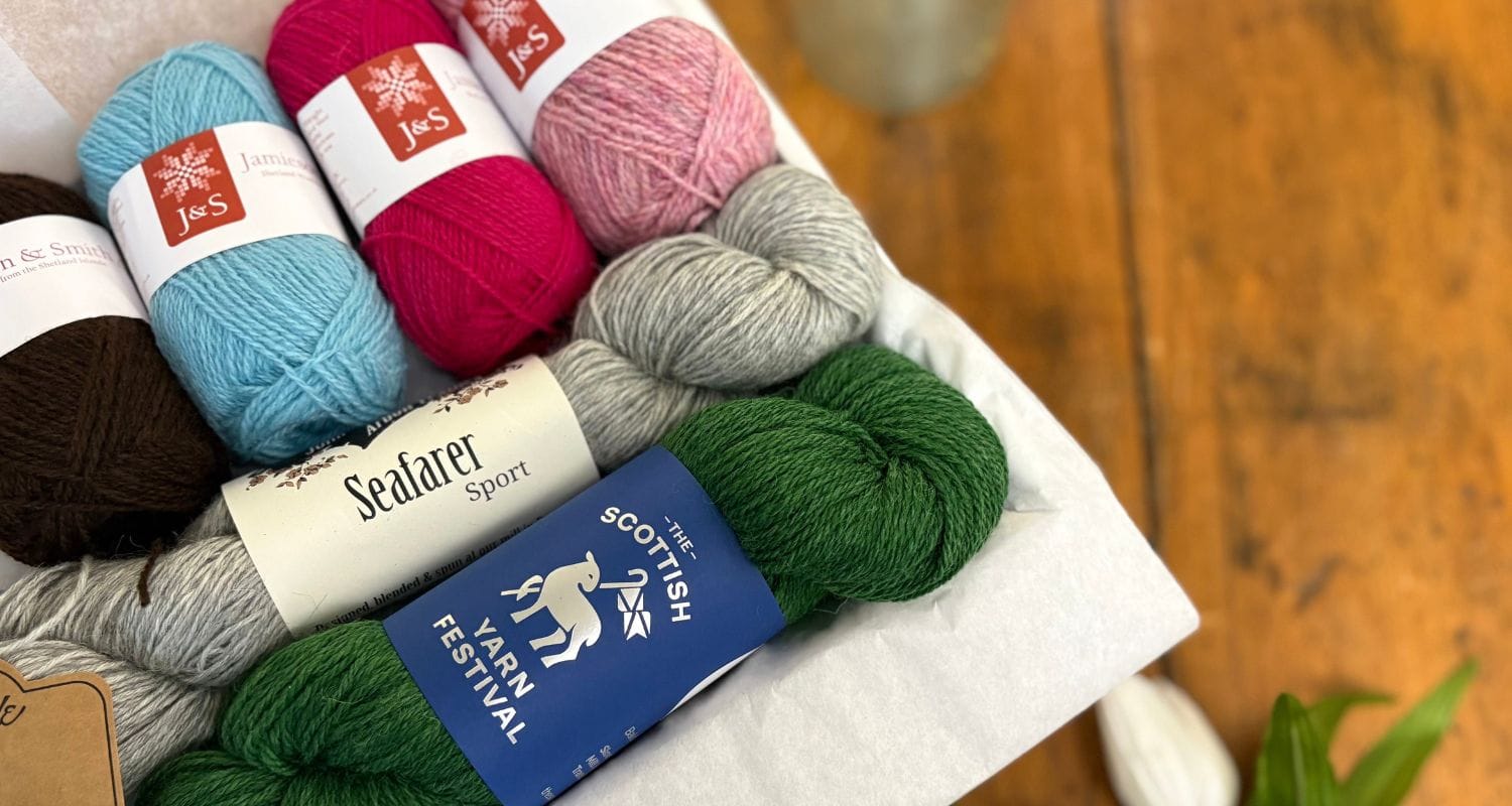 Colorful skeins of yarn with visible brand labels on a wooden surface. Three yarns shown that are included in the Spring Taster Box.
