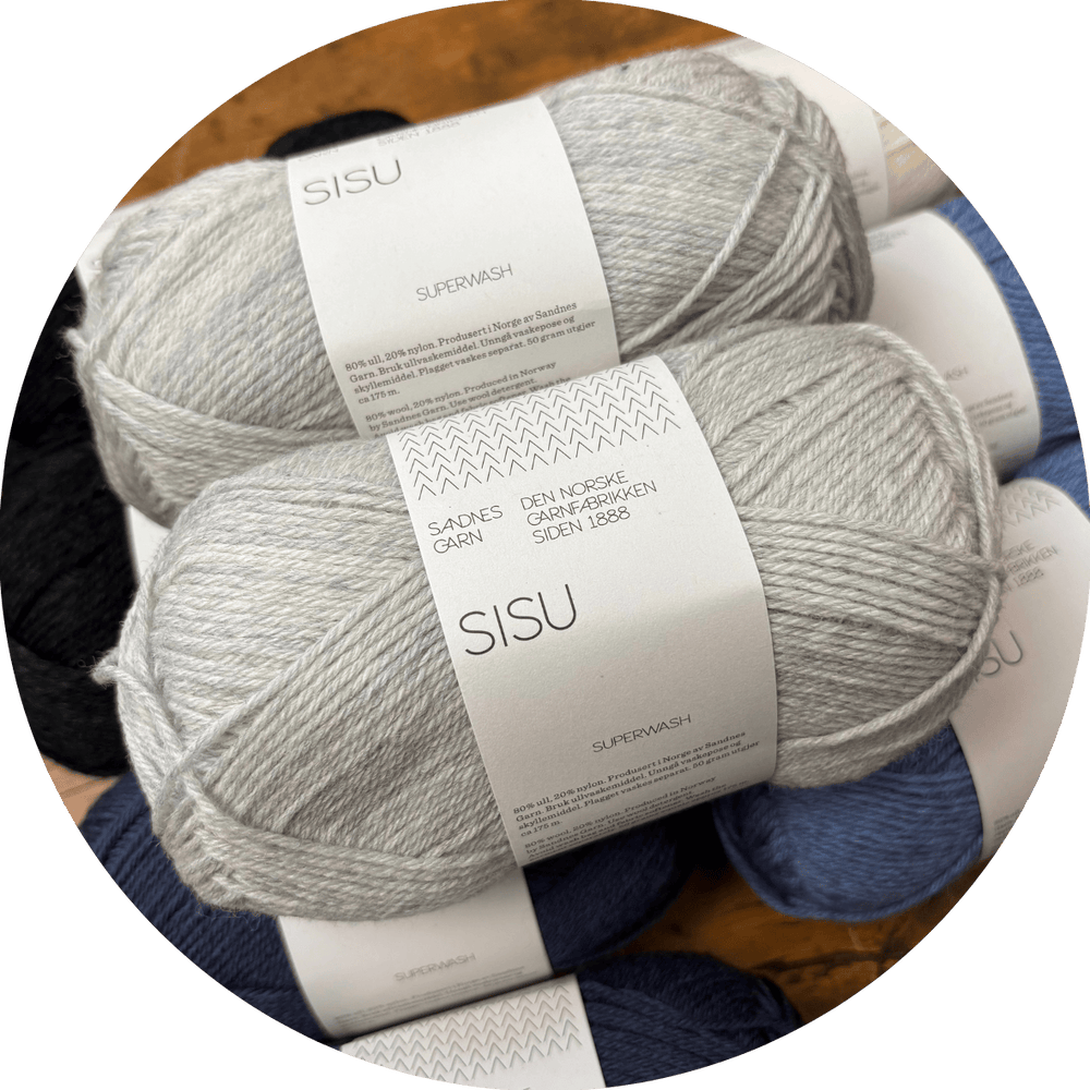 Two skeins of light grey Sandness Garn SISU yarn with labels on a blurred background of other yarn colros.