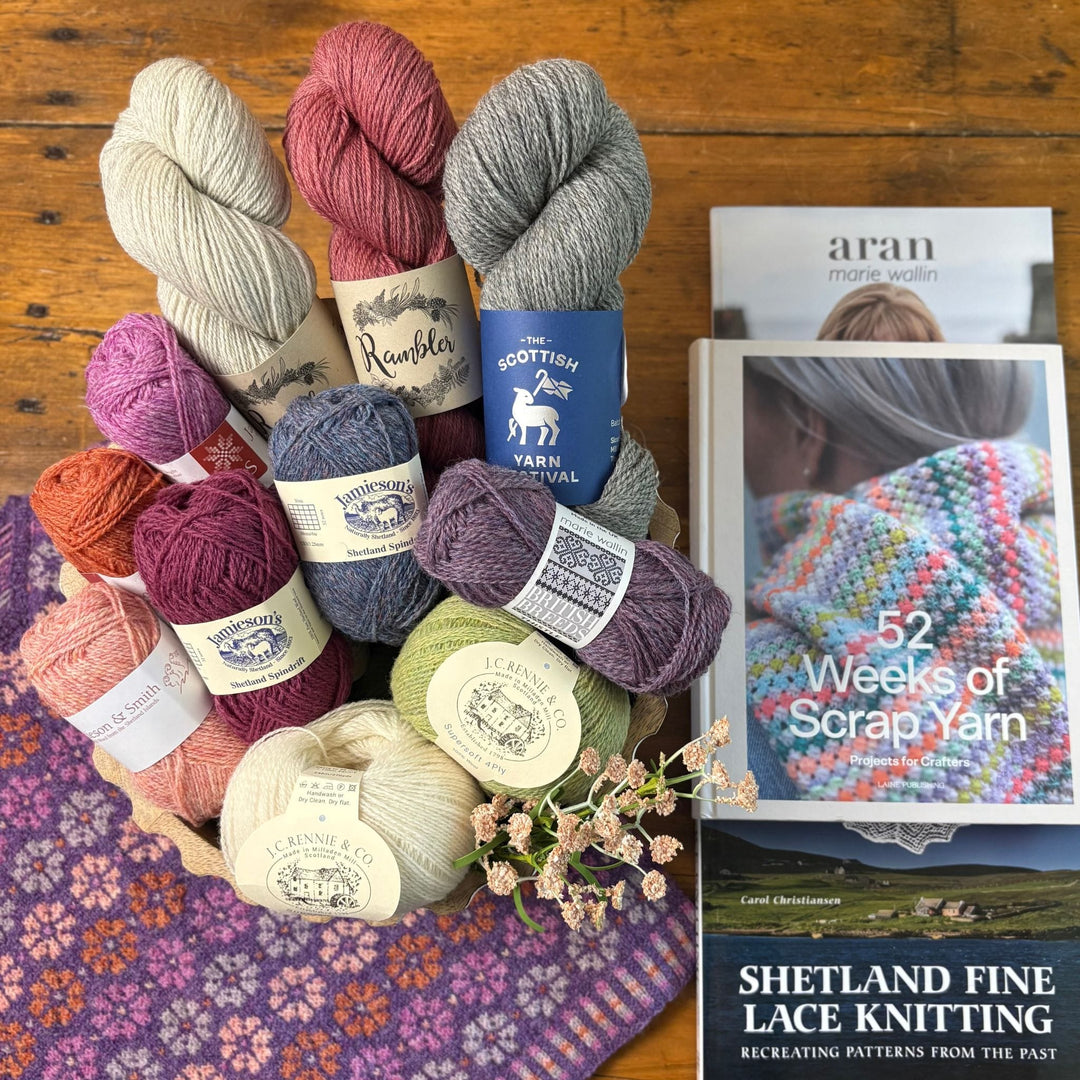 Shetland yarn in a basket overtop a colorwork knit fabric and books displayed with Shetland themes.