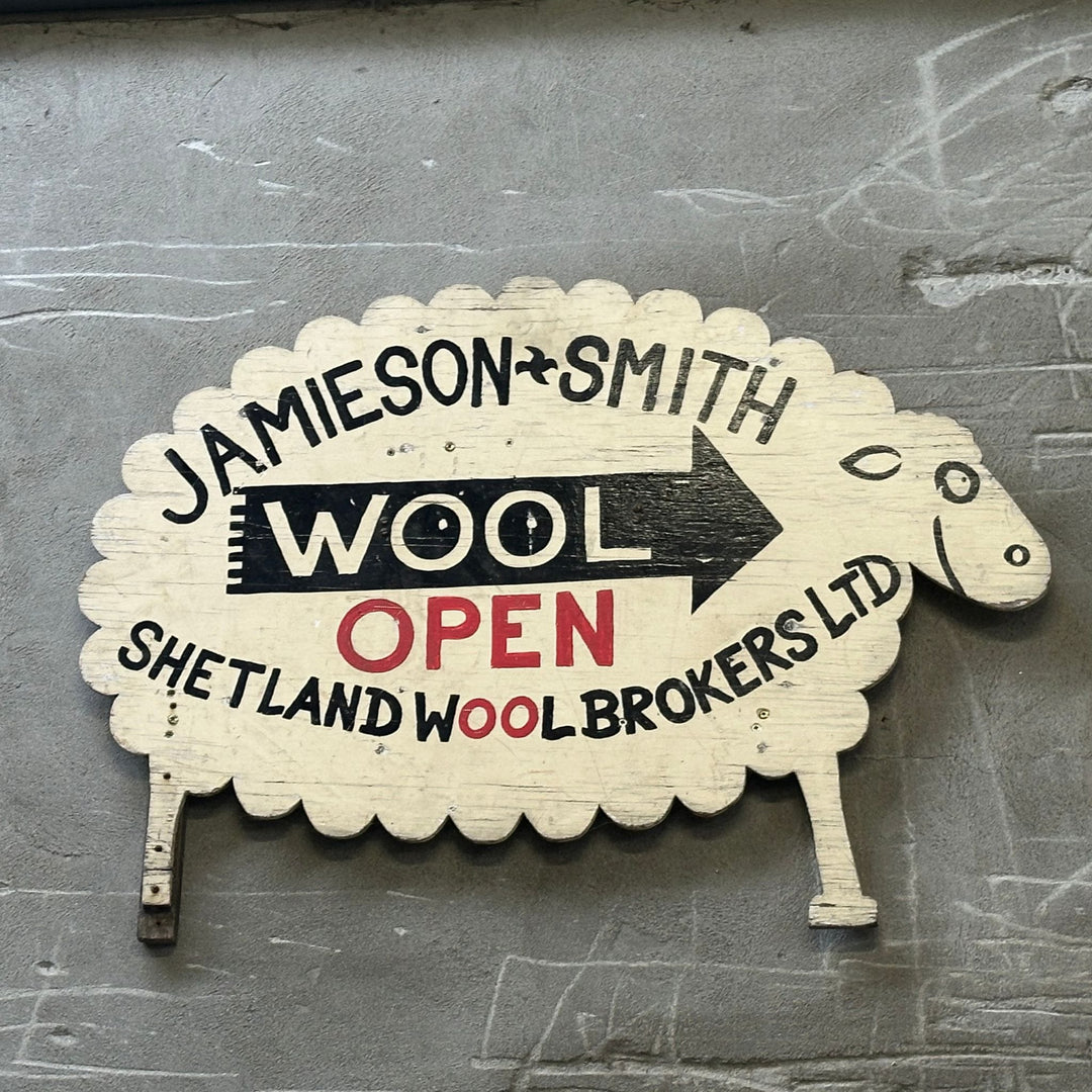 Wooden sheep-shaped sign with text 'Jamieson Smith Wool Open Shetland Wool Brokers Ltd' on a textured surface.