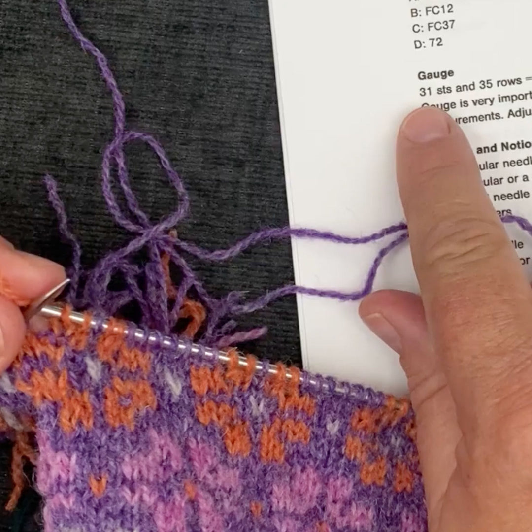 finger pointing to text 'gauge 31 sts' text while knitting a swatch