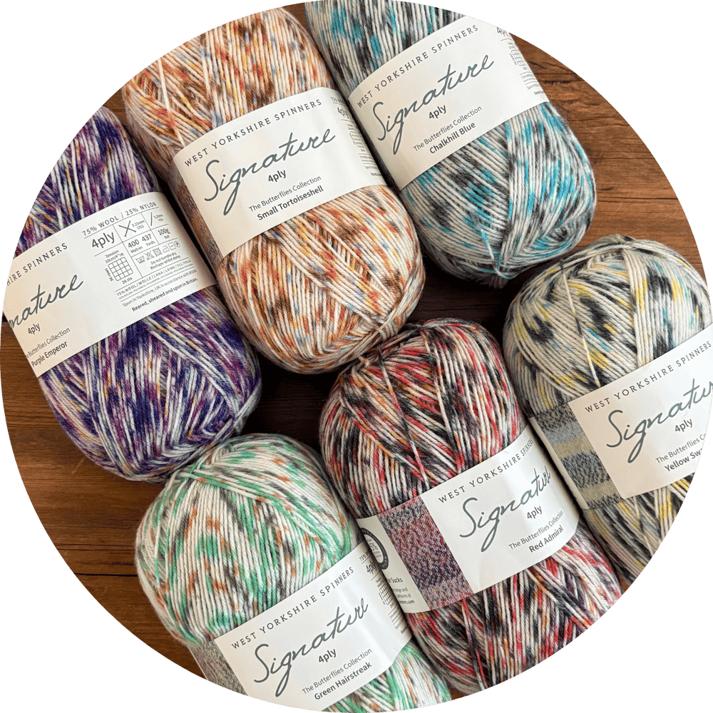 Colorful, variegated yarn balls with labels on a wooden surface. Six balls are West Yorkshire Spinners Signature 4ply in the Butterflies colorway collection.
