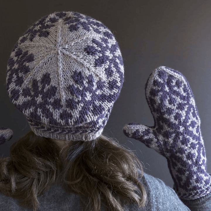 Designer Virginia Sattler-Reimer wearing Overwinter Mittens and Tam knit with Briggs & Little Yarn standing against dark background showing crown of Tam. 