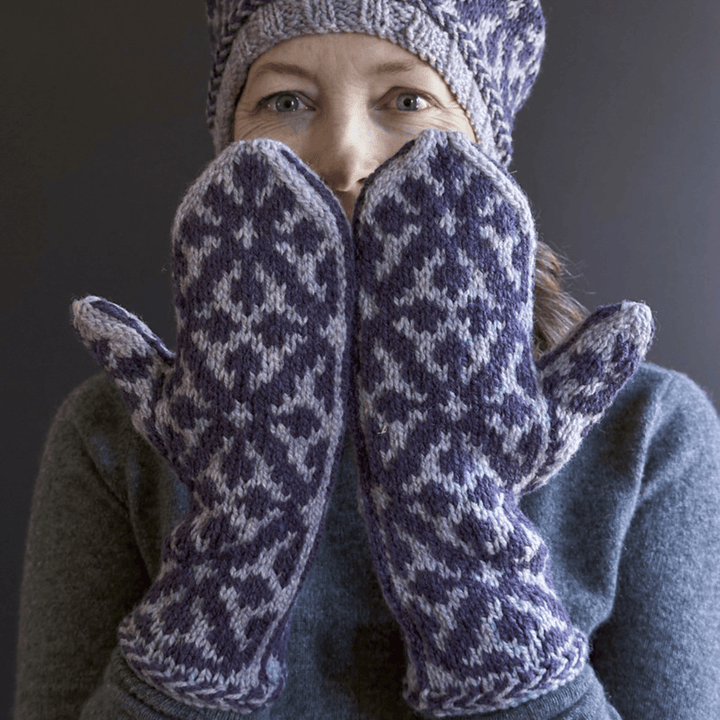 Designer Virginia Sattler-Reimer wearing Overwinter Mittens and Tam knit with Briggs & Little Yarn standing against dark background. 