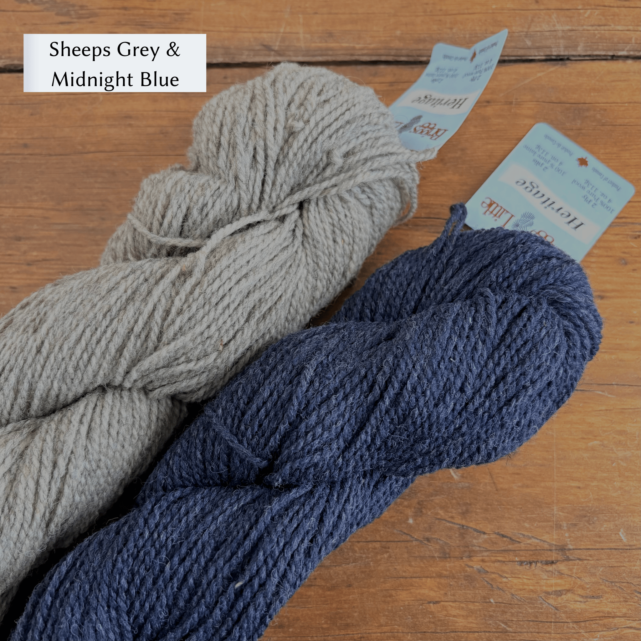Two skeins of yarn, one gray and one blue, on a wooden surface with labels. Yarn set designed to knit Overwinter Mittens and Tam designed by Virginia Sattler-Reimer. 