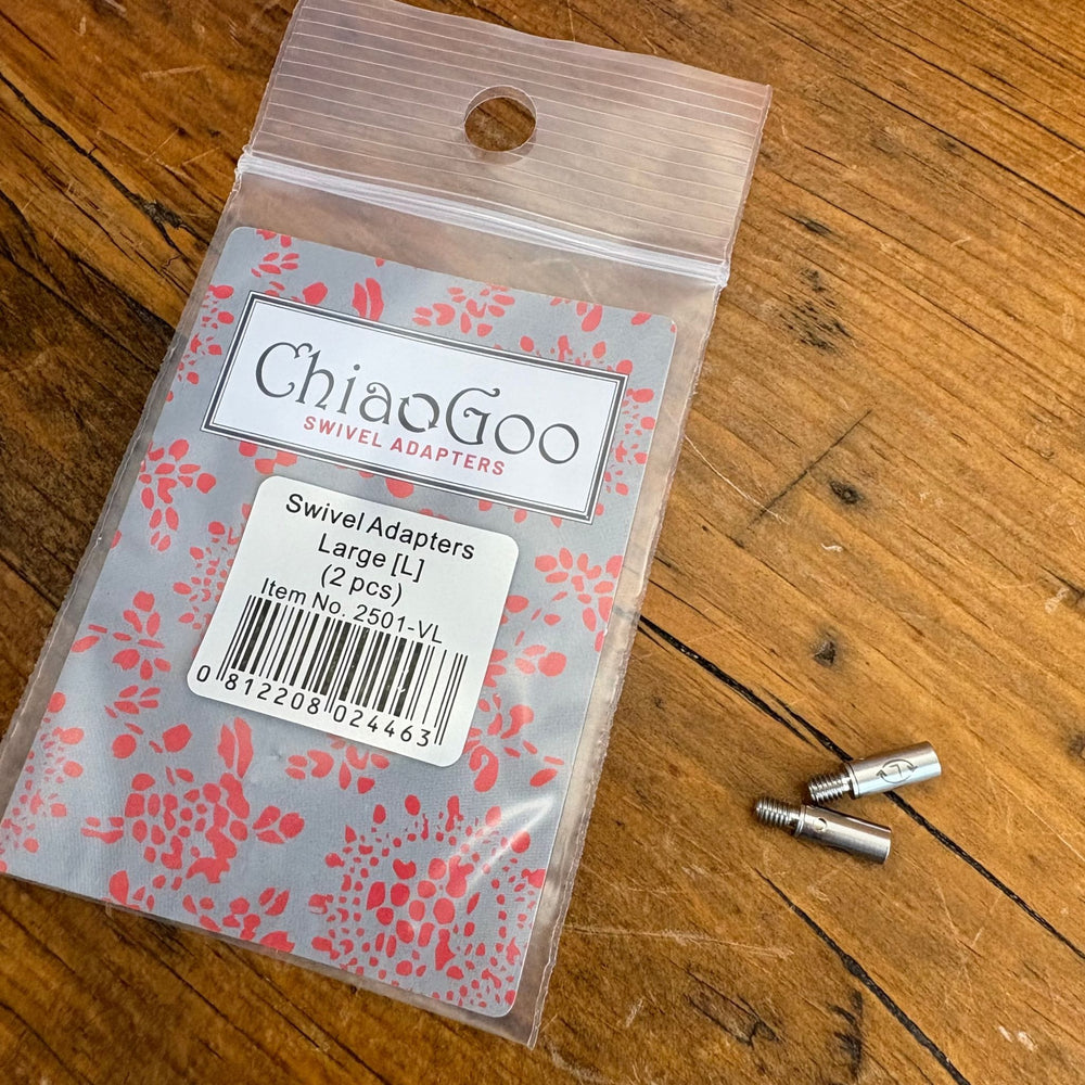 ChiaoGoo swivel adapters packaging on a wooden surface shown at an angle with the 2 large swivel adapters next to the package. 