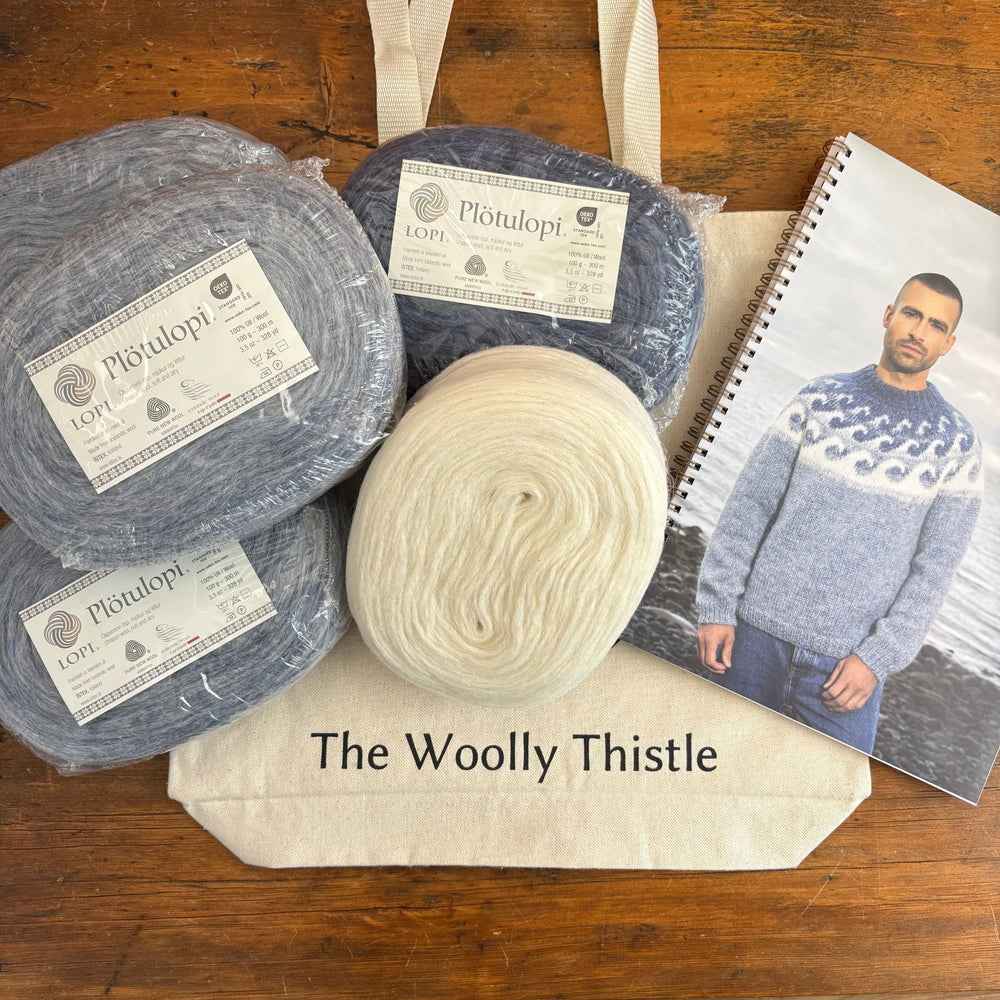 Plotulopi yarn with labels on a wooden surface, next to a photo featuring a man wearing a blue sweater, the Brimskafl by Vedis Jonsdottir. The Woolly Thistle tote bag under yarn and book. 