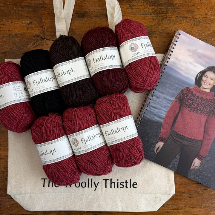 Red and black yarn skeins with 'Fjallalopi' labels on a wooden surface, next to a photo of a person wearing a red sweater. Sweater design is the Dalaeti by Vedis Jonsdottir.