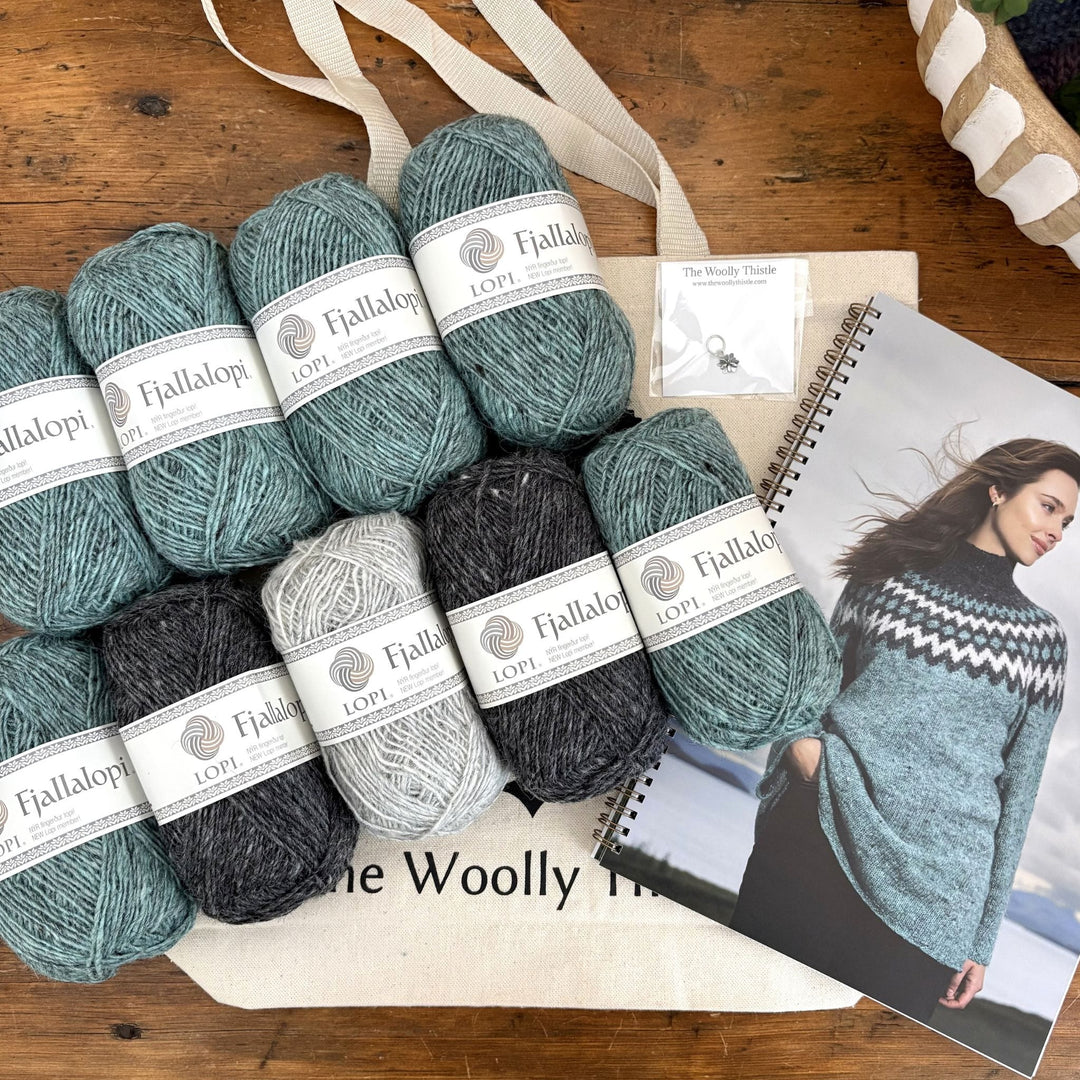 Flat lay of Fjallalopi yarn for the Holt Sweater in coordinating colors with TWT tote, stitch marker, and pattern book.