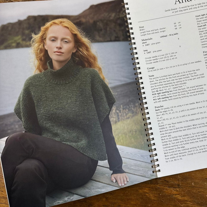 Page from Lopi Book 45 Autumn shows Woman wearing a green knitted poncho sitting by a lake, with a knitting pattern book open next to her.