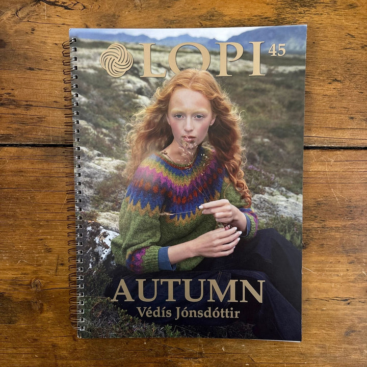 Spiral bound Book titled 'LOPI 45 Autumn' featuring a woman in a colorful sweater on a wooden surface.