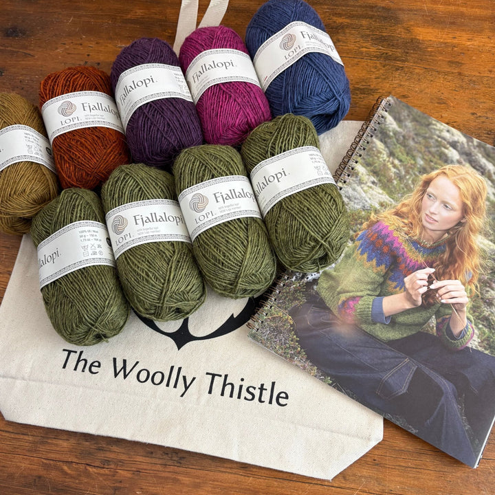 Collection of Fjallalopi yarn balls with labels on a wooden surface next to an image of a person wearing a colorful sweater called Mói. Yarn and photo are on top of The Woolly Thistle branded tote bag. 