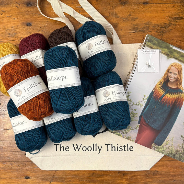 Flat Lay of Tigla by Védís Jónsdóttir kit with Fjallalopi yarn balls, pattern booklet, stitch marker, and branded tote bag shown atop a wooden surface.