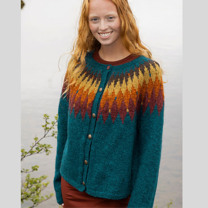 Front view of Tigla cardigan in Fjallalopi, showing teal body and bold stranded colorwork yoke shown on woman in outdoor setting.