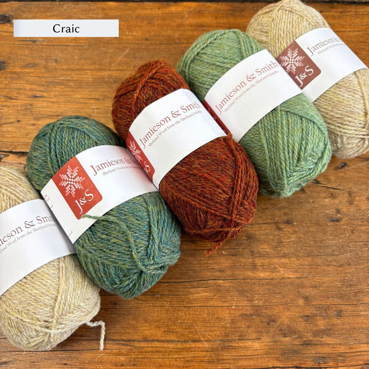 Yarn balls with 'Jameson & Smith' labels on a wooden surface labeled Craic. Beige, green, and maroon yarn used to knit the lighter colorway of the Shamrock Hat.