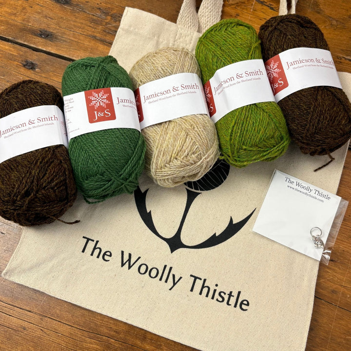 Four balls of yarn in brown, green, and beige on a 'The Woolly Thistle' branded bag. Jamieson & Smith yarn to knit the Shamrock Hat in dark colorway.