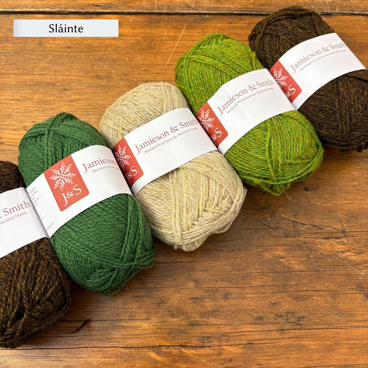 Four skeins of yarn in green, beige, and brown on a wooden surface with 'Sláinte' text above. Jamieson & Smith yarn in greens and neutrals to knit the Shamrock Hat.