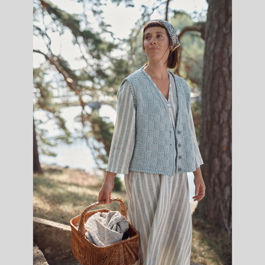 Photo from Laine Issue 28 of a woman in a light blue, textured vest and striped pants holding a picnic basket in a park.