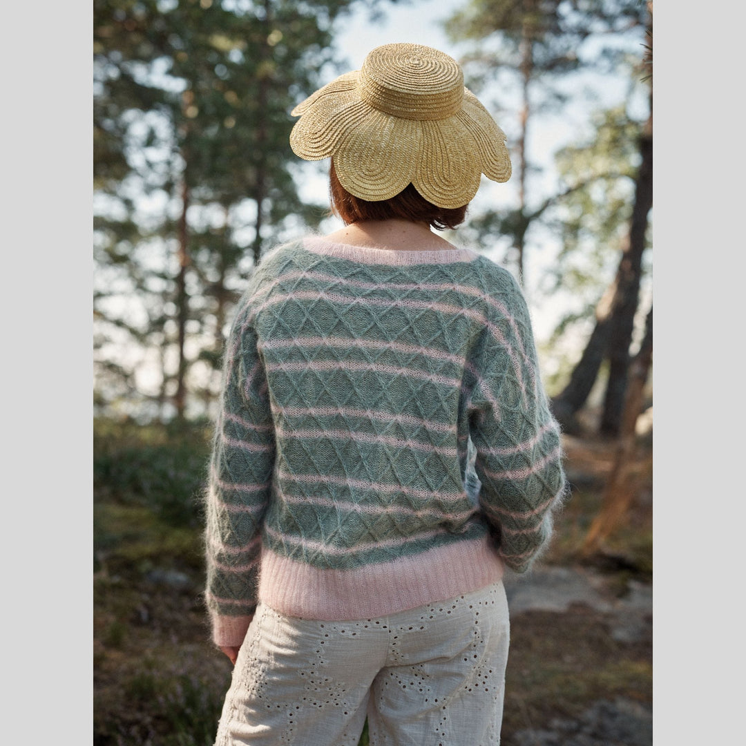 Photo from Laine Issue 28 of a person wearing a striped and textured, blue and pink sweater and straw hat in a forest setting