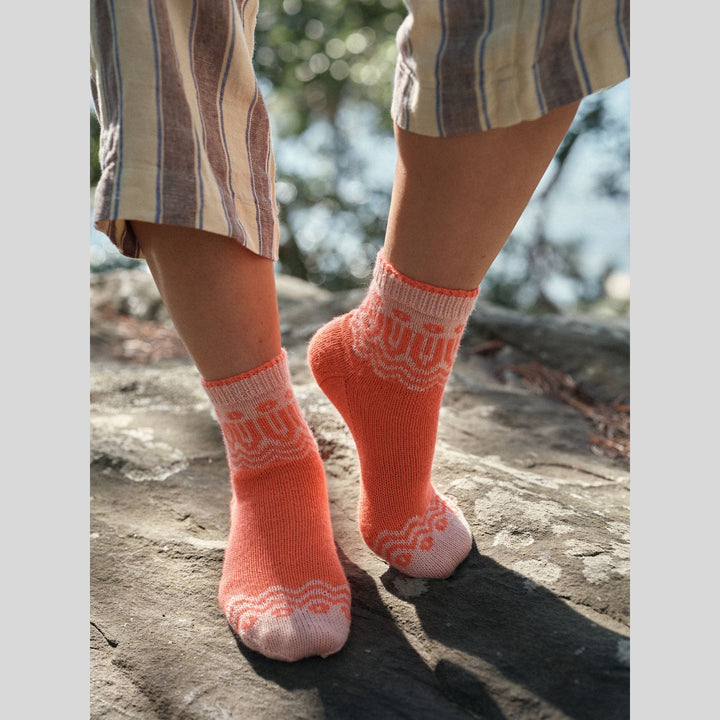 Photo from Laine Issue 28 person's legs and feet wearing orange socks with white patterns standing on a stone surface.