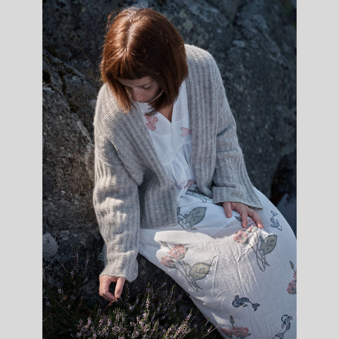 Photo from Laine Issue 28 of woman sitting on rocks wearing a light gray cardigan and floral dress.