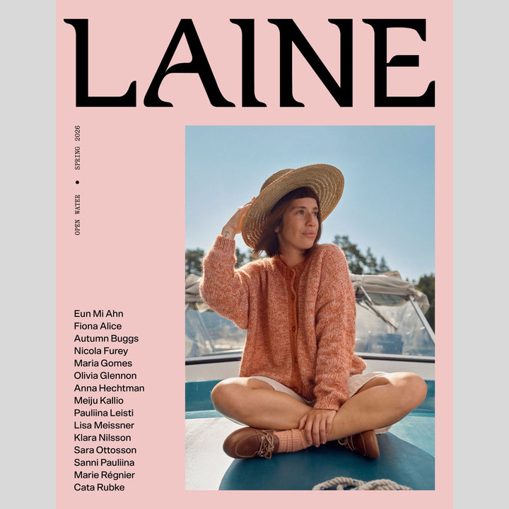 Laine 28 magazine cover with a woman sitting on a boat, wearing a straw hat and orange sweater, against a pink background with list of contributing designers. 