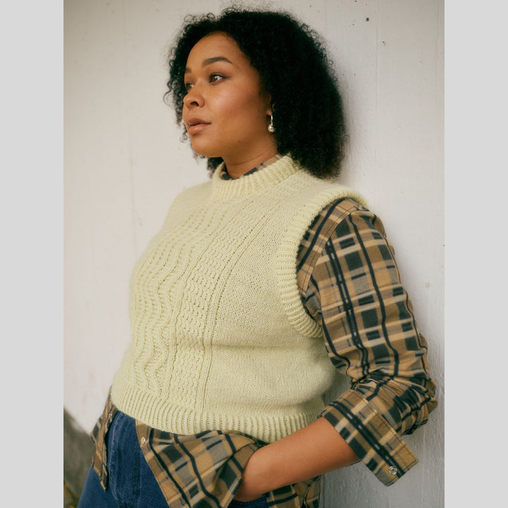 From Laine book My City, My Stitches sold at The Woolly Thistle pages show Woman wearing a cream knitted sweater over a plaid shirt against a white wall