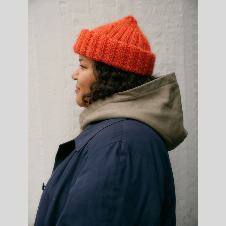 From Laine book My City, My Stitches sold at The Woolly Thistle pages show a person wearing a bright orange knit beanie and dark blue jacket against a light gray background
