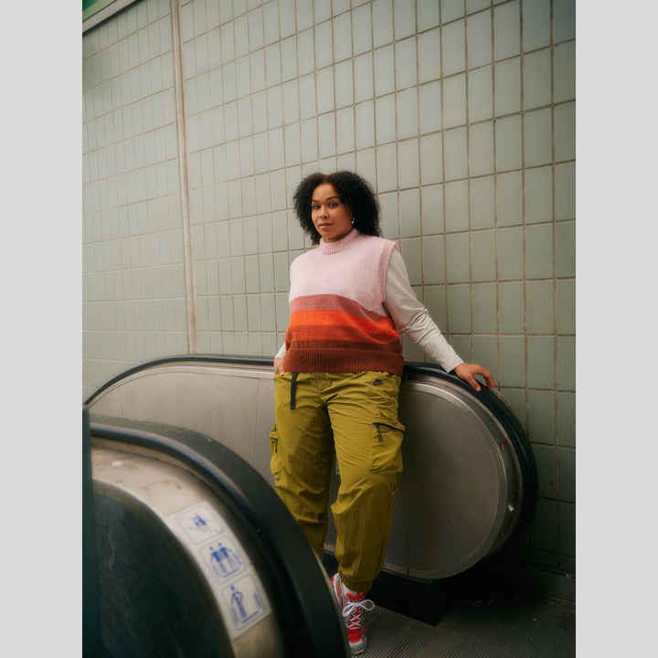 From Laine book My City, My Stitches sold at The Woolly Thistle page shows person wearing a colorful knit vest and yellow pants leaning against a wall.