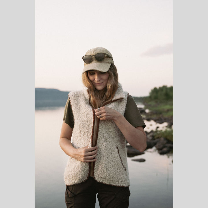 Woman wearing a beige fleece vest and cap by a lake. This is a page from Laine Book "Unfolding Landscapes"