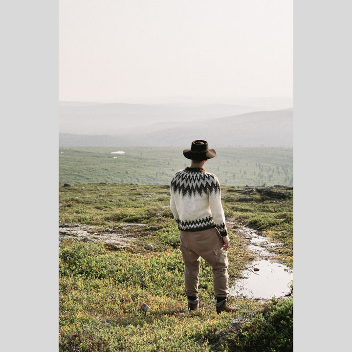 Person wearing a patterned sweater and hat standing in a grassy field. This is a page from Laine Book "Unfolding Landscapes"