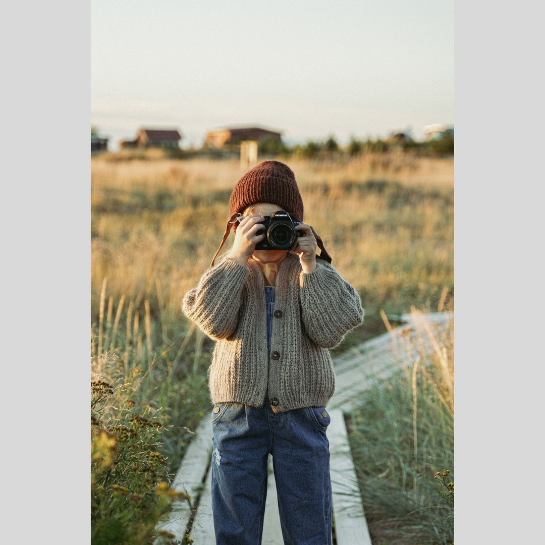 Child taking a photo in a field wearing a beanie and cardigan. This is a page from Laine Book "Unfolding Landscapes"