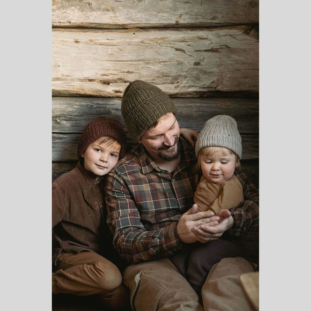 Man with two children wearing knit hats sitting against a wooden wall. This is a page from Laine Book "Unfolding Landscapes"