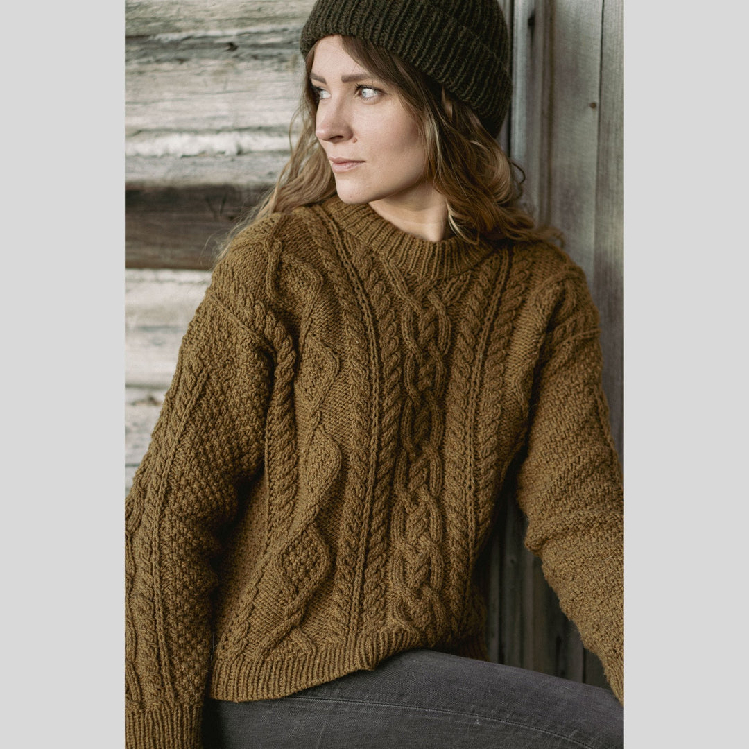 Woman wearing a brown knitted sweater and green beanie against a wooden background. This is a page from Laine Book "Unfolding Landscapes"