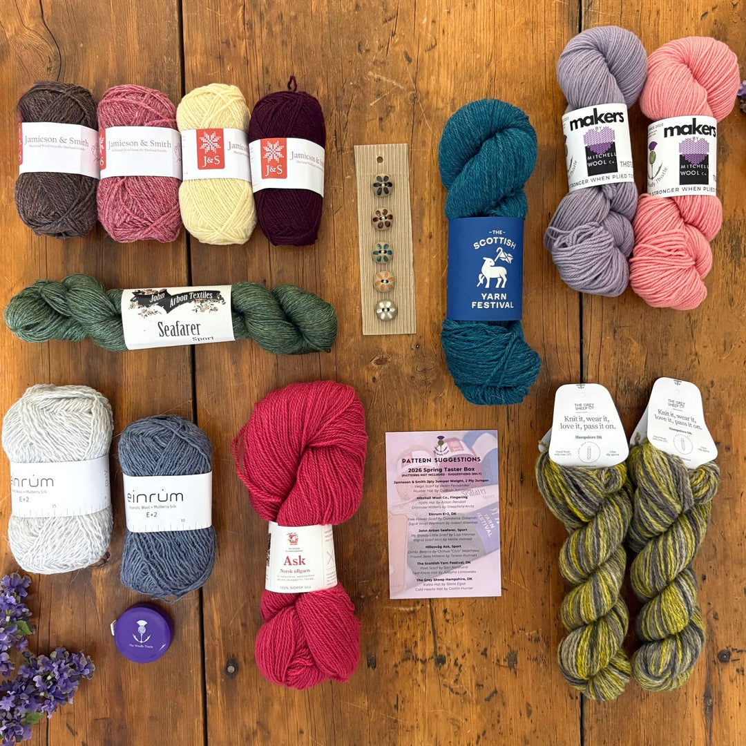 All the yarns included in the Spring Taster Box arranged on a wooden surface. 720g of wool in various colorful skeins and balls. 