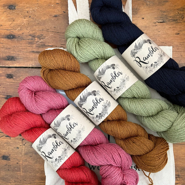 Assorted skeins of yarn in a range of colors, arranged diagonally with 'Rambler' labels on a wooden surface