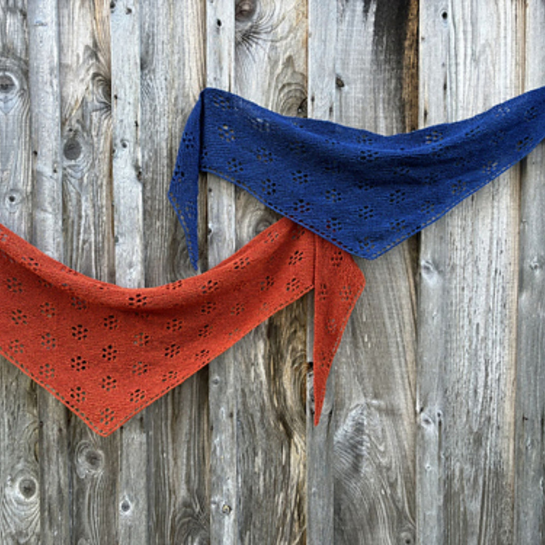 Red and blue knitted shawls draped on a wooden background. Shawl design is Ghost Flowers Shawl by Amy Christoffers.