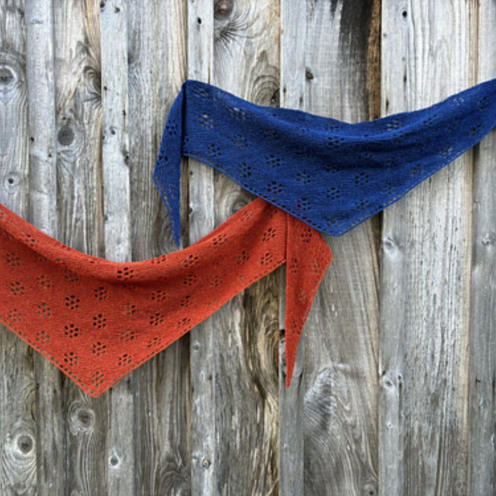 Red and blue knitted shawls draped on a wooden background. Shawl design is Ghost Flowers Shawl by Amy Christoffers.