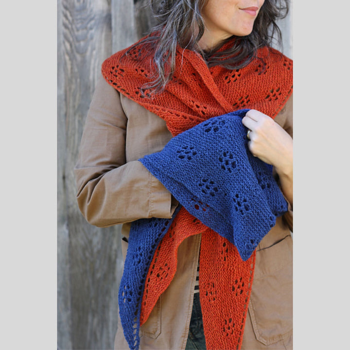 Person wearing a red knitted shawl and a blue knitted shawl is on her arm. Shawl design is Ghost Flowers Shawl by Amy Christoffers.