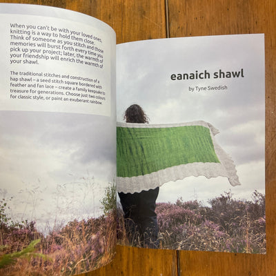 Perspectives book edited by Julie Rutter & Emily K. Williams. Pages open to photo of the Eanaich Shawl, knit in green and cream, being held by a woman standing in field. Opposite page provides more information about the shawl.