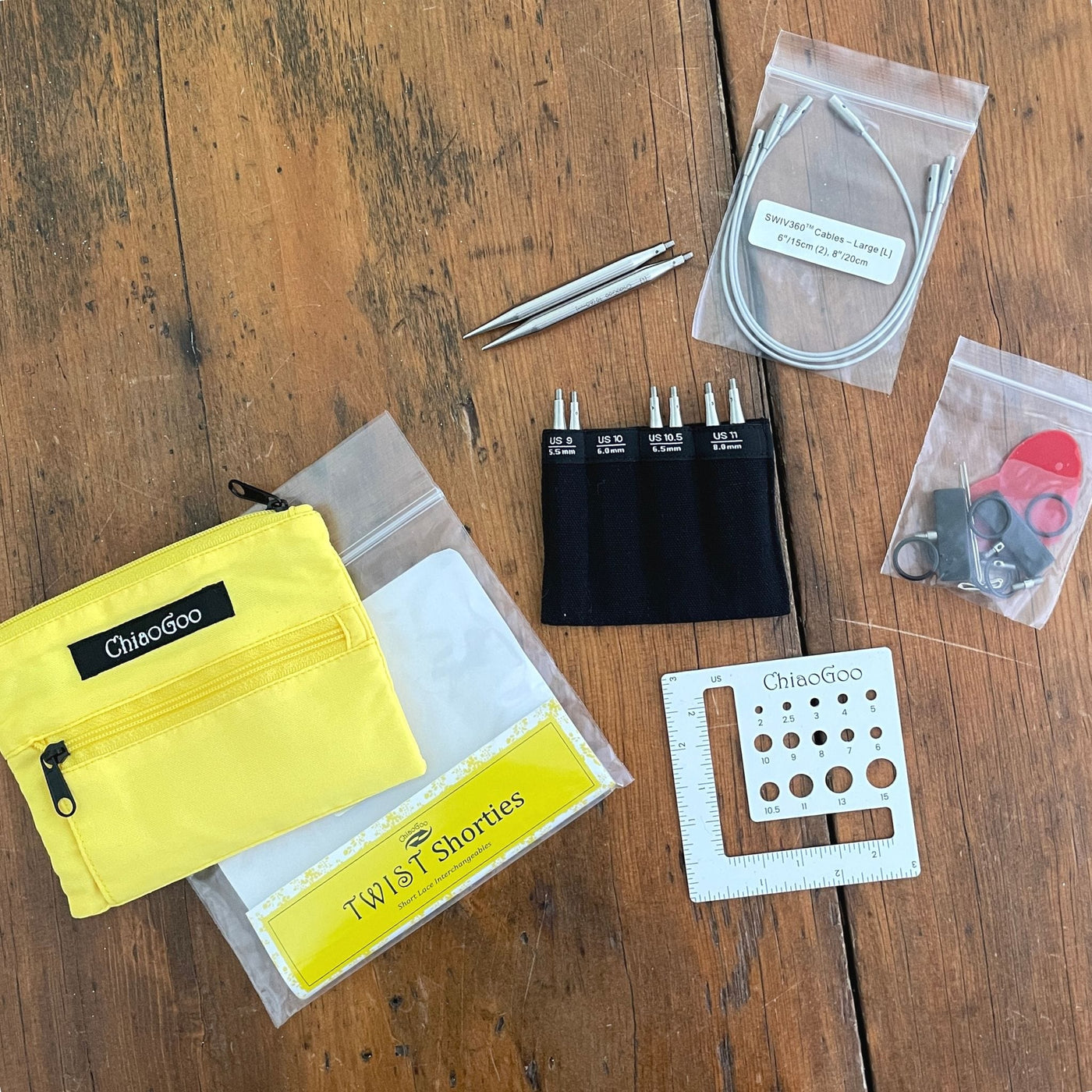 Chiaogoo 3" Twist Large Shortie set. Shown with all components on wood background with yellow pouch. Needle tips in US 9, 10, 10.5, 11, Connectors, 3 cables, end stoppers, tightening key, rubber gripper, stitch markers, and needle gauge.